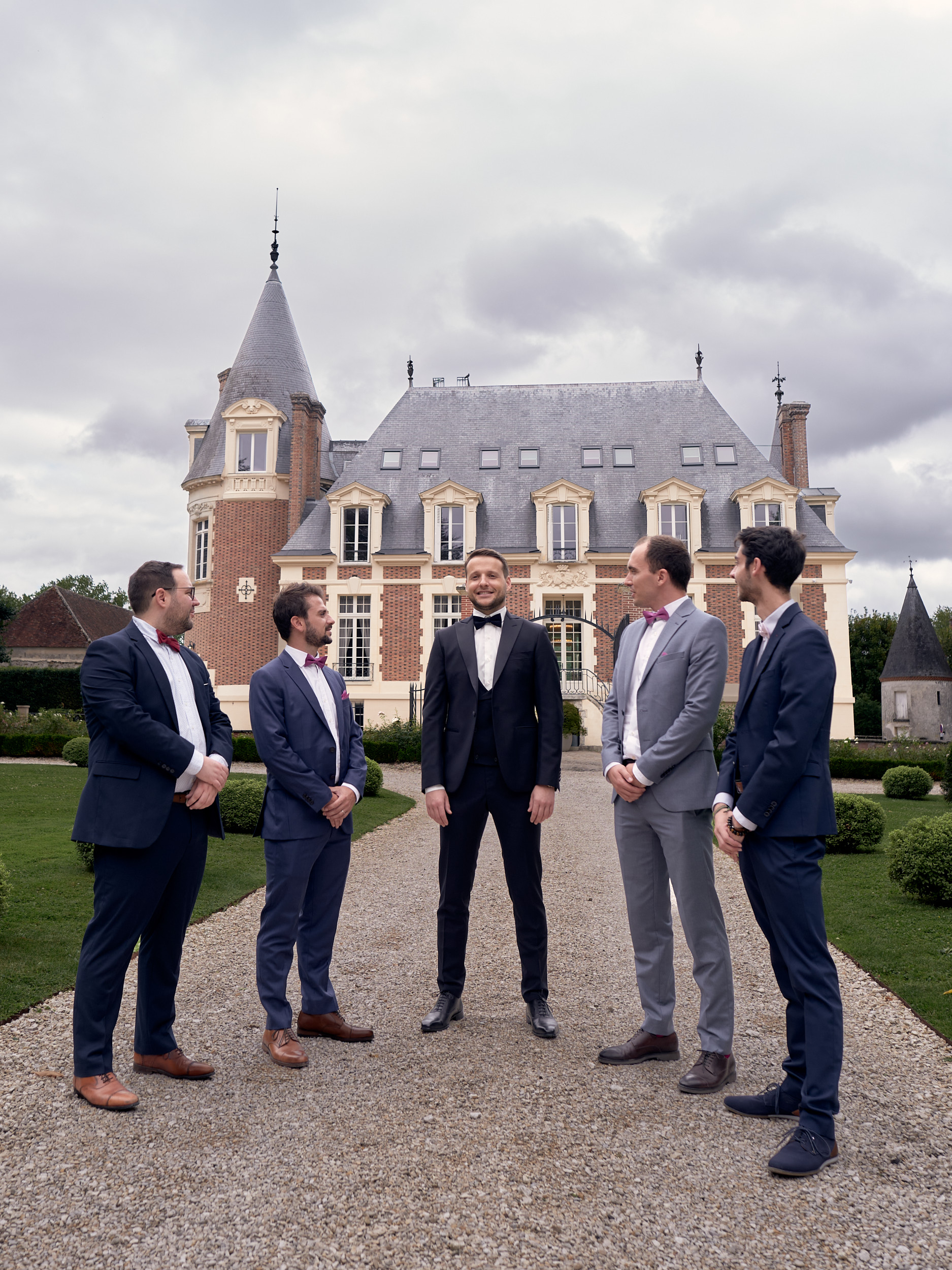 Marié entouré de quatre hommes en costume sur une allée devant un château.