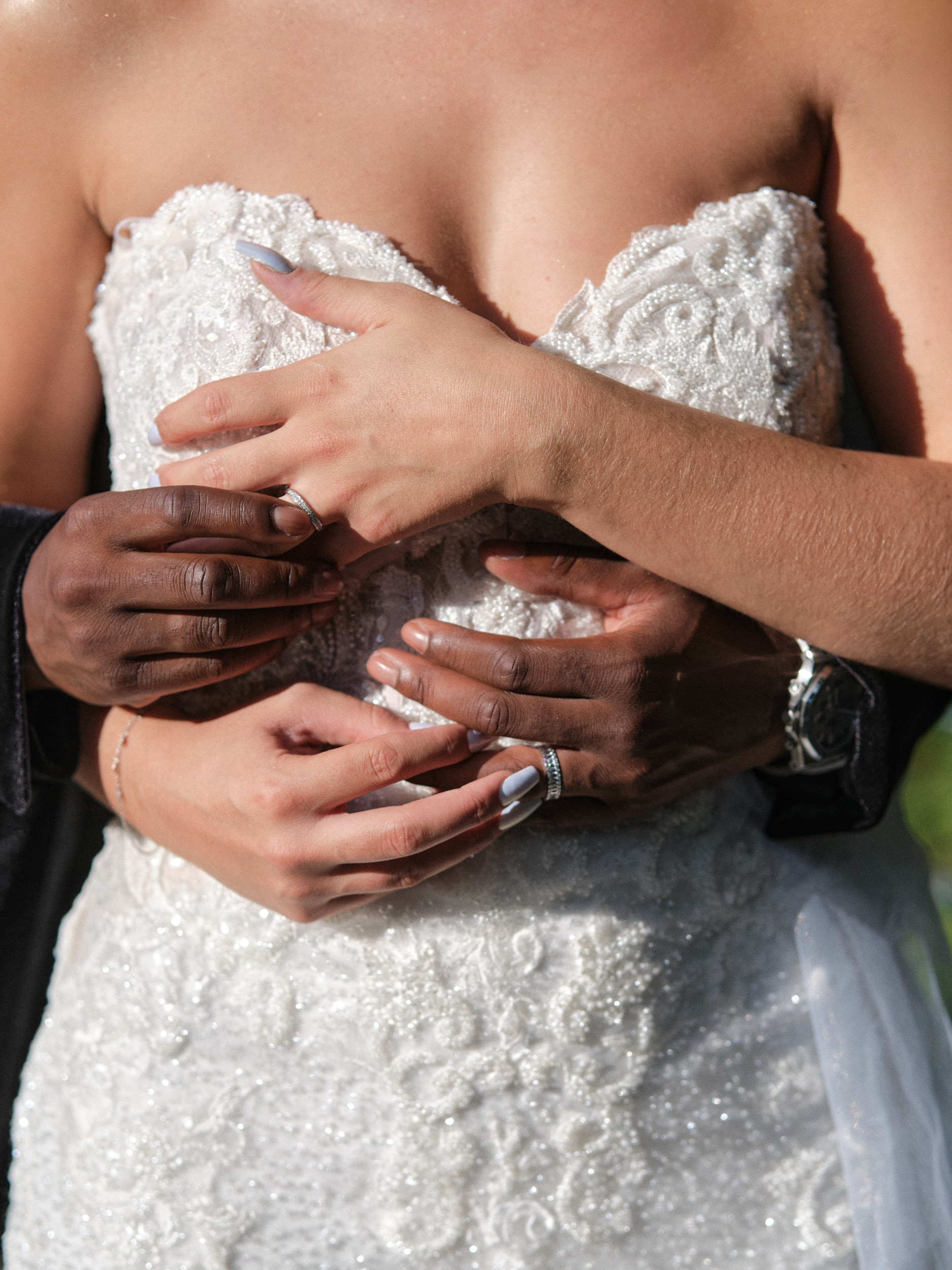 Gros plan des mains des mariés enlacées sur le corsage brodé de la robe de mariée.