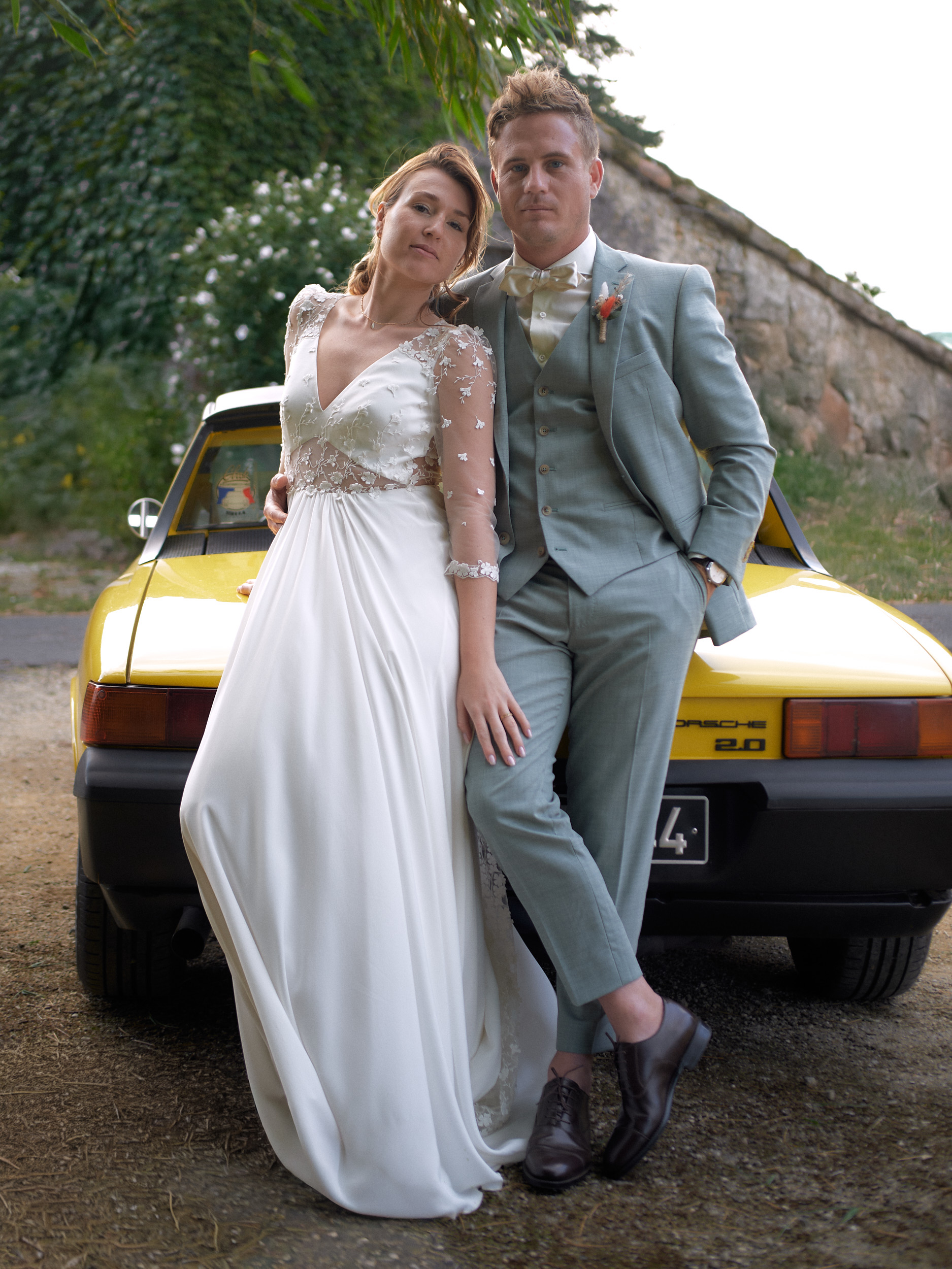 Mariés appuyés contre une voiture jaune, la mariée posant la tête sur l’épaule du marié.