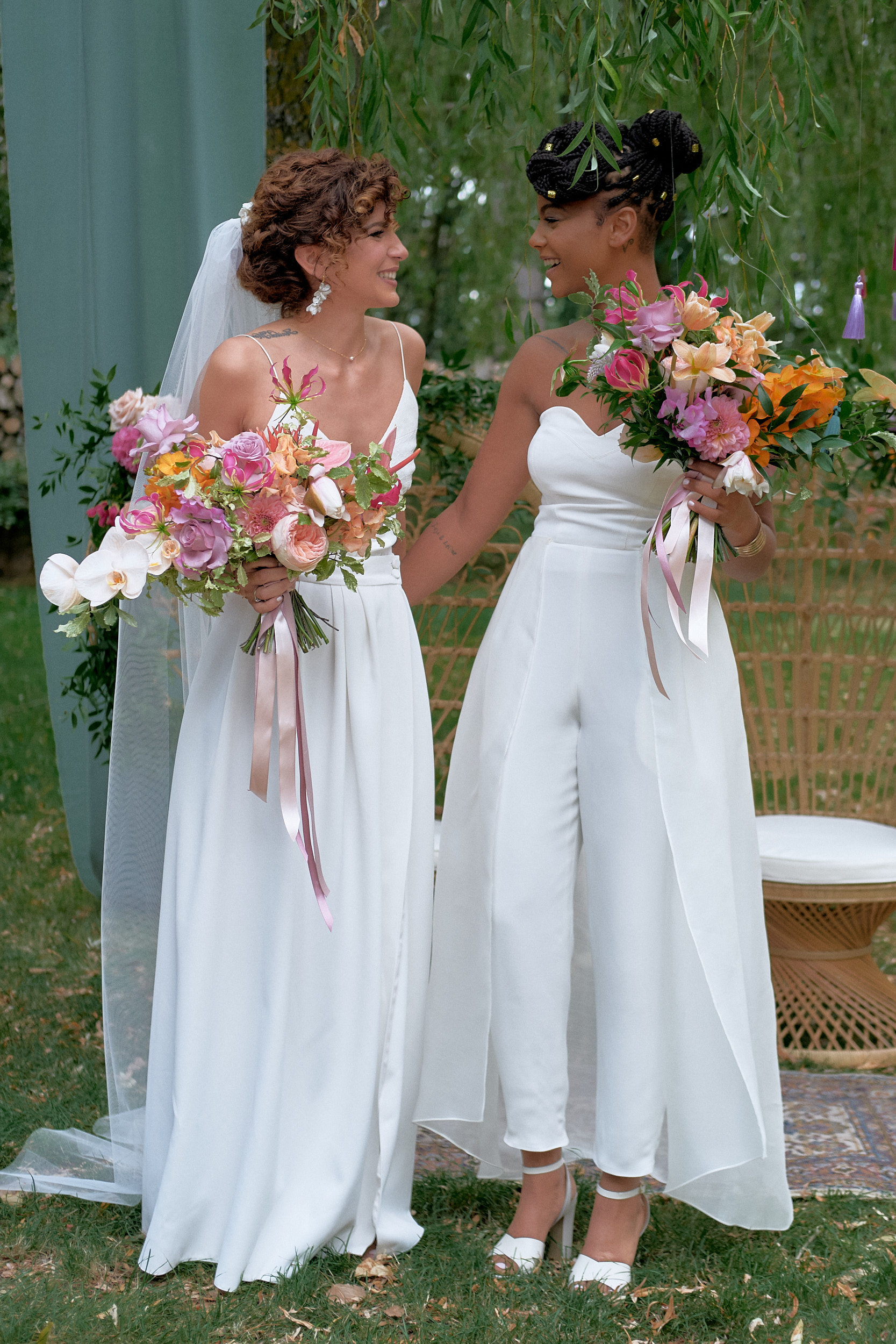 Deux mariées se regardant et tenant des bouquets colorés dans un jardin.