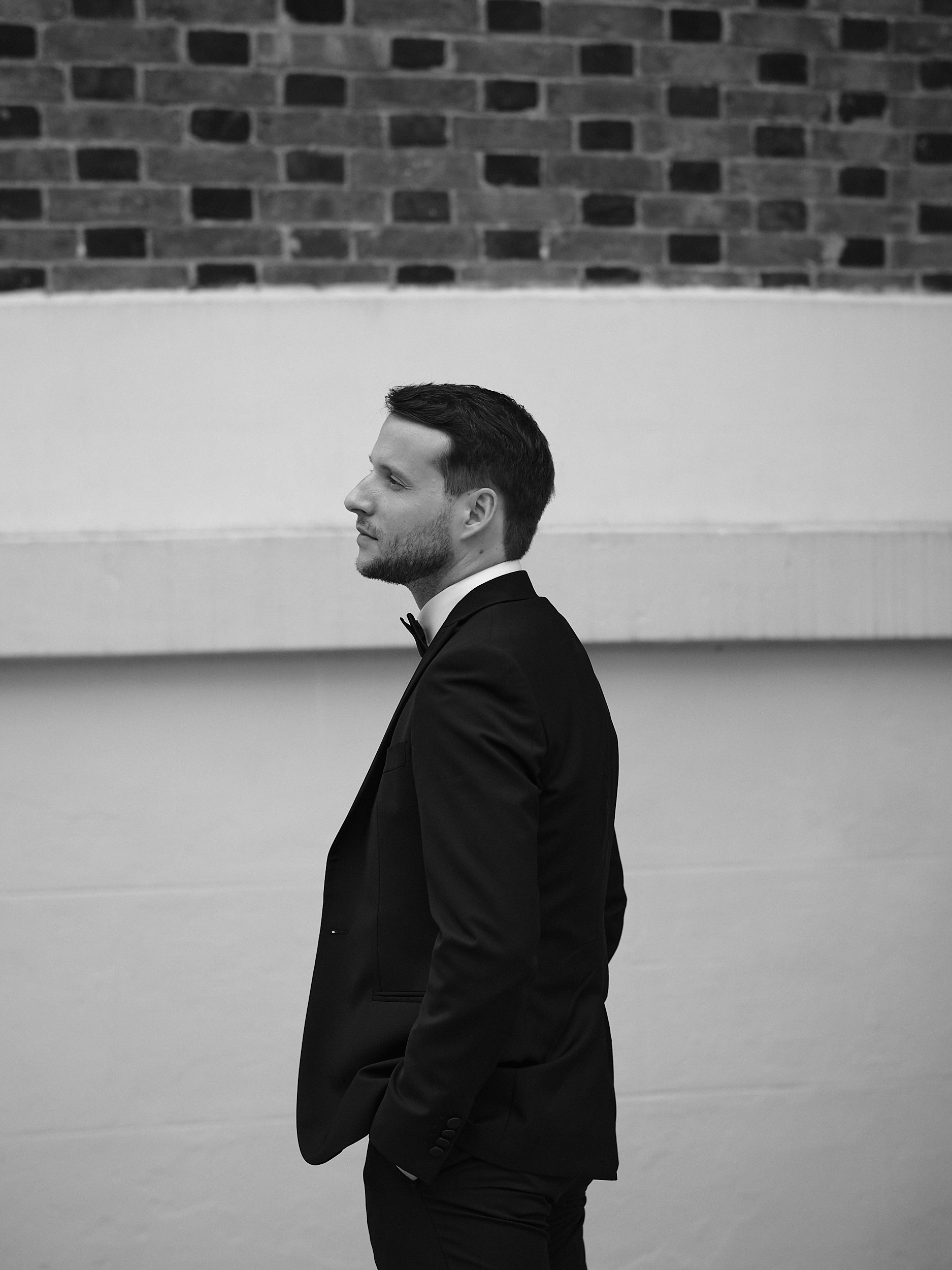 Portrait de profil du marié en costume sombre et nœud papillon, en noir et blanc.