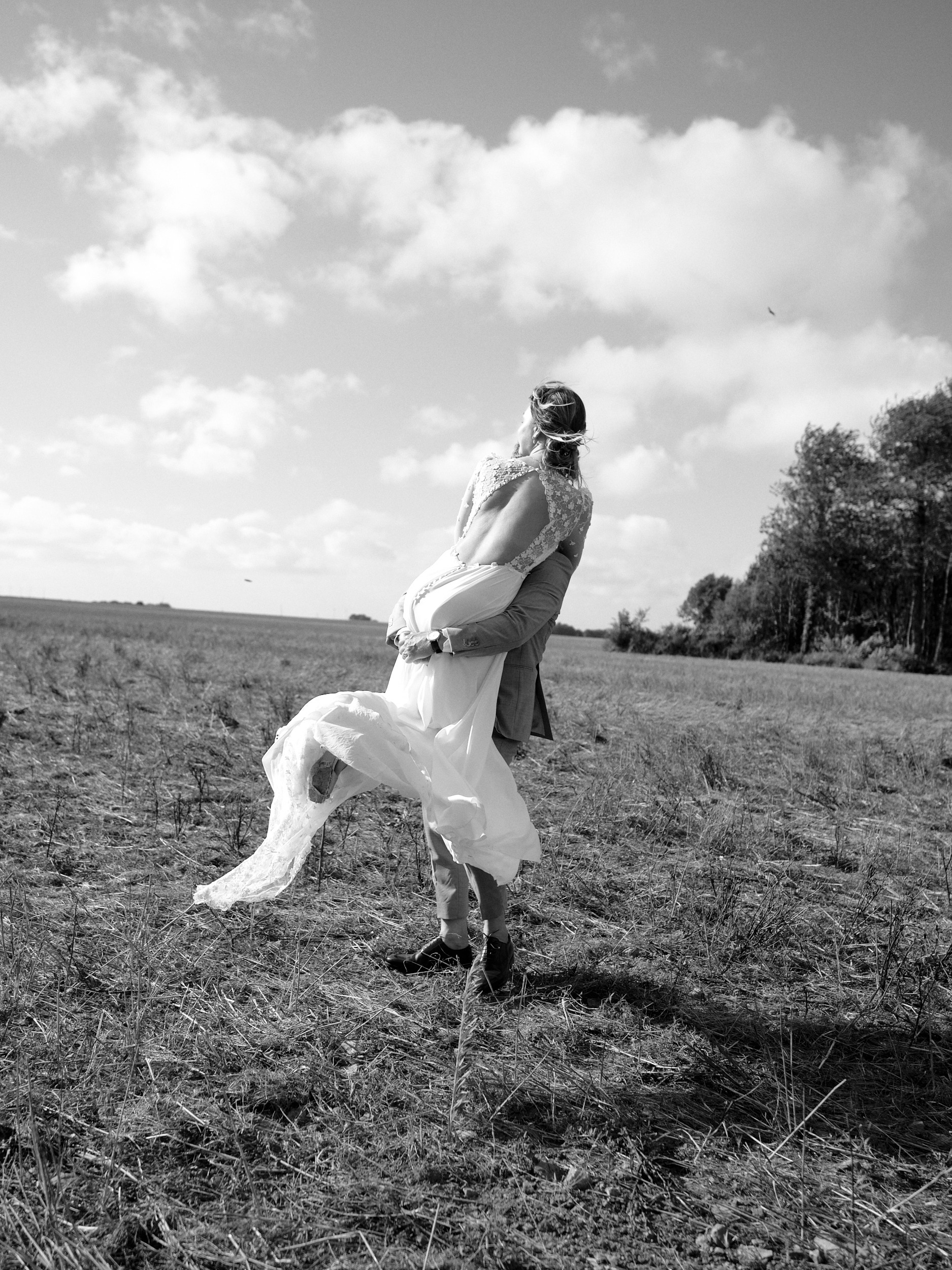 Marié portant la mariée dans un champ, en noir et blanc.