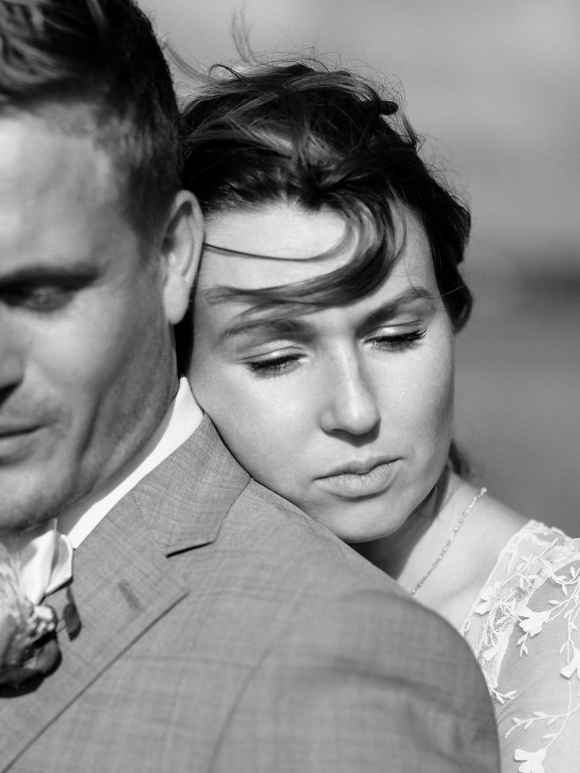 Gros plan en noir et blanc de la mariée posant son visage contre l’épaule du marié.