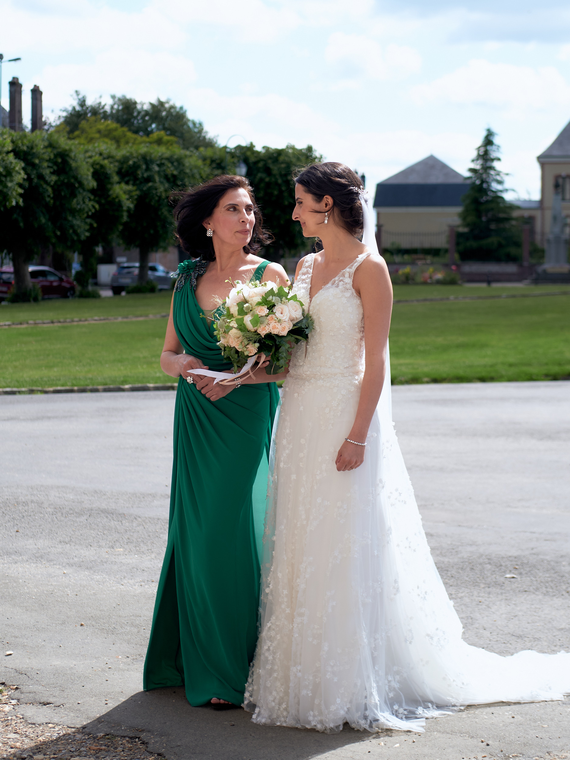 Mariée et femme en robe verte se regardant, un bouquet entre elles.